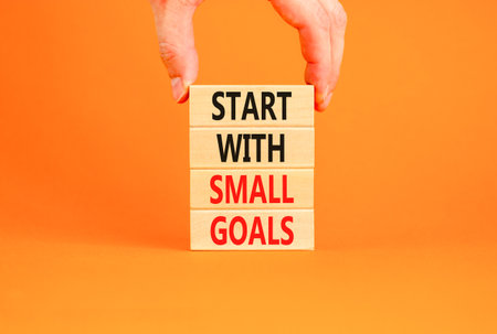 Start with small goals symbol. Concept words phrase Start with small goals on beautiful wooden blocks. Beautiful orange background Businessman hand Business Start with small goals concept. Copy space.の写真素材