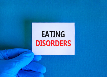 Eating disorders symbol. Concept words Eating disorders on beautiful white card. Doctor's hand in blue medical glove. Beautiful blue background. Medical healthy lifestyle eating disorders concept.の写真素材