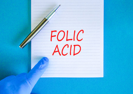 Folic acid symbol. Concept words Folic acid on beautiful white note. Doctor's hand in blue medical glove. Black pen. Beautiful blue background. Medical healthy lifestyle folic acid concept.の写真素材