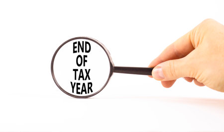 End of tax year symbol. Concept words phrase End of tax year in beautiful black magnifying glass. Businessman's hand. Beautiful white background. Business End of tax year concept. Copy space.の写真素材