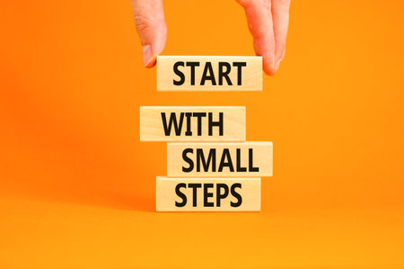 Start with small steps symbol. Concept words phrase Start with small steps on beautiful wooden blocks. Beautiful orange background. Businessman hand Business Start with small steps concept. Copy spaceの写真素材