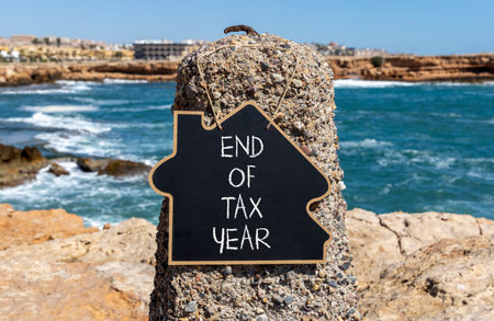 End of tax year symbol. Concept words phrase End of tax year on beautiful black blackboard. Beautiful stone blue sea sky background. Business End of tax year concept. Copy space.の写真素材