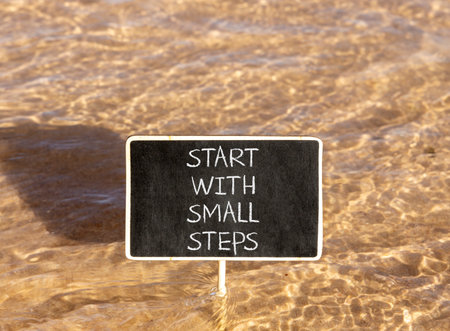 Start with small steps symbol. Concept words phrase Start with small steps on beautiful black blackboard. Beautiful Red sea water background. Business Start with small steps concept. Copy space.の写真素材