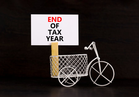 End of tax year symbol. Concept words phrase End of tax year on beautiful white paper on wooden clothespin. Bicycle. Beautiful black paper background. Business End of tax year concept. Copy space.の写真素材