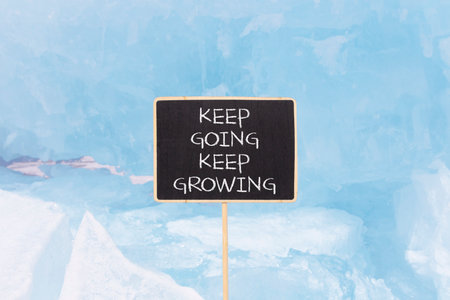 Keep going and growing symbol. Concept words phrase Keep going keep growing on beautiful black blackboard. Beautiful blue ice background. Business Keep going and growing concept. Copy space.の写真素材