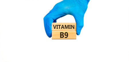 Vitamin B9 folic acid symbol. Concept words Vitamin B9 on beautiful wooden blocks. Doctor's hand in blue medical glove. Beautiful white background. Medical healthy lifestyle Vitamin B9 concept.の写真素材
