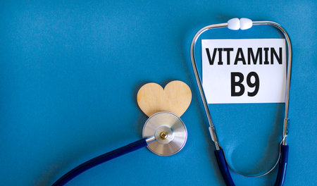 Vitamin B9 folic acid symbol. Concept words Vitamin B9 on beautiful white card. Wooden heart and stethoscope. Beautiful blue background. Medical healthy lifestyle Vitamin B9 concept.の写真素材