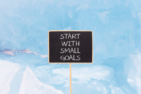 Start with small goals symbol. Concept words phrase Start with small goals on beautiful black blackboard. Beautiful blue ice background. Business Start with small goals concept. Copy space.の写真素材