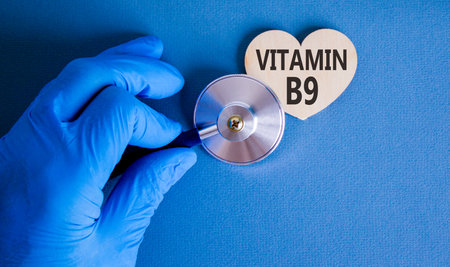 Vitamin B9 folic acid symbol. Concept words Vitamin B9 on beautiful wooden heart. Doctor's hand in blue medical glove. Beautiful blue background. Medical healthy lifestyle Vitamin B9 concept.の写真素材