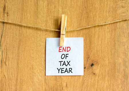 End of tax year symbol. Concept words phrase End of tax year on beautiful white paper on wooden clothespin. Beautiful wooden background. Business End of tax year concept. Copy space.の写真素材