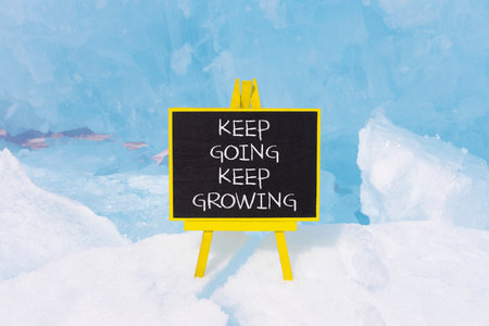 Keep going and growing symbol. Concept words phrase Keep going keep growing on beautiful black blackboard. Beautiful blue ice background. Business Keep going and growing concept. Copy space.の写真素材