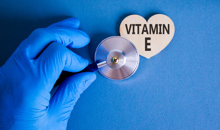 Vitamin E tocopherols symbol. Concept words Vitamin E on beautiful wooden heart. Doctor's hand in blue medical glove. Beautiful blue background. Medical healthy lifestyle Vitamin E tocopherols conceptの写真素材