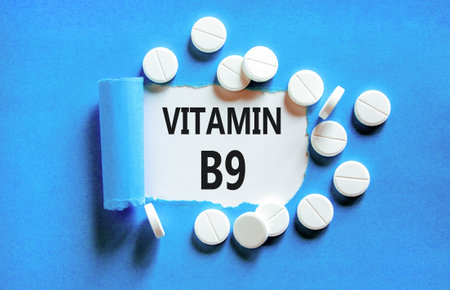 Vitamin B9 folic acid symbol. Concept words Vitamin B9 on beautiful white paper. White pills tablets. Beautiful blue background. Medical healthy lifestyle Vitamin B9 concept.の写真素材
