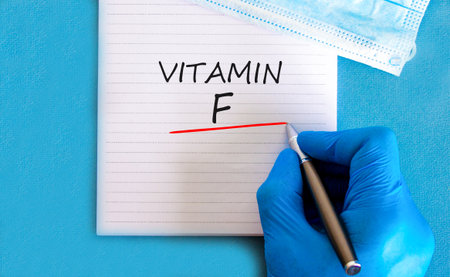 Vitamin F symbol. Concept words Vitamin F on beautiful white note. Doctor's hand in blue medical glove. Medical mask. Beautiful blue background. Medical healthy lifestyle Vitamin F concept.の写真素材