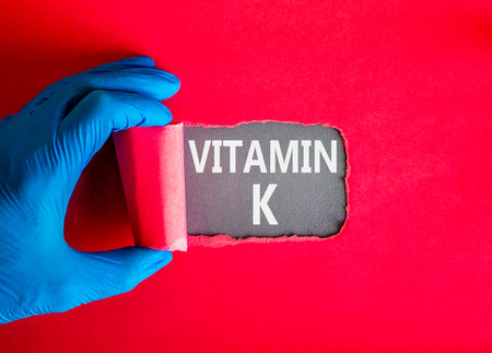 Vitamin K phylloquinone symbol. Concept words Vitamin K on beautiful gray paper. Doctor hand in blue medical glove. Beautiful red background. Medical healthy lifestyle Vitamin K phylloquinone concept.の写真素材