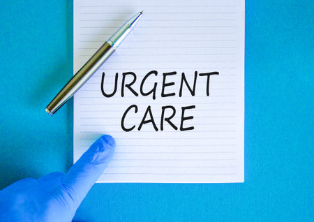 Urgent care symbol. Concept words Urgent care on beautiful white note. Doctor's hand in blue medical glove. Black pen. Beautiful blue background. Medical healthy lifestyle urgent care concept.の写真素材