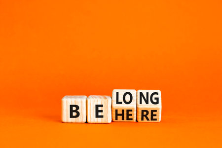 Belonging and belong symbol. Concept words Be here Belong on beautiful wooden block. Beautiful orange table orange background. Business motivational belonging and belong concept. Copy space.の写真素材