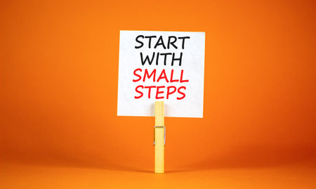 Start with small steps symbol. Concept words phrase Start with small steps on beautiful white paper on clothespin. Beautiful orange background. Business Start with small steps concept. Copy space.の写真素材