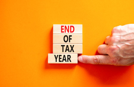 End of tax year symbol. Concept words phrase End of tax year on beautiful wooden blocks. Beautiful orange paper background. Businessman's hand. Business End of tax year concept. Copy space.の写真素材