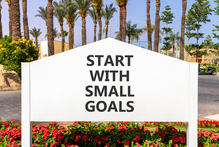 Start with small goals symbol. Concept words phrase Start with small goals on beautiful white road sign. Beautiful palm tree blue sky background. Business Start with small goals concept. Copy space.の写真素材