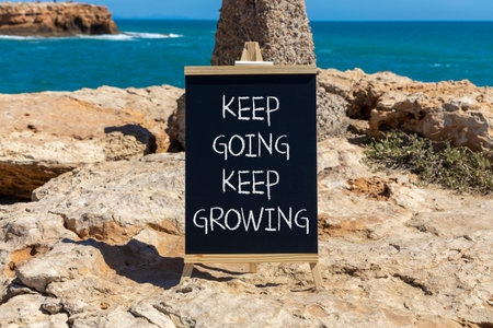 Keep going and growing symbol. Concept words phrase Keep going keep growing on beautiful black blackboard. Beautiful stone blue sea sky background. Business Keep going and growing concept. Copy space.の写真素材