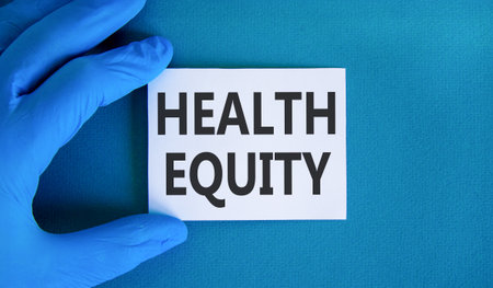 Health equity symbol. Concept words Health equity on beautiful white card. Doctor's hand in blue medical glove. Beautiful blue background. Medical healthy lifestyle health equity concept.の写真素材
