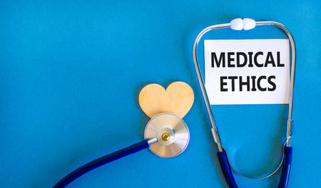 Medical ethics symbol. Concept words Medical ethics on beautiful white card. Wooden heart and stethoscope. Beautiful blue background. Medical healthy lifestyle medical ethics concept.の写真素材