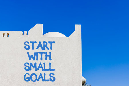 Start with small goals symbol. Concept words phrase Start with small goals on beautiful white wall. Beautiful white wall and blue sky background. Business Start with small goals concept. Copy space.の写真素材