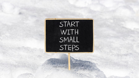 Start with small steps symbol. Concept words phrase Start with small steps on beautiful black blackboard. Beautiful white snow background. Business Start with small steps concept. Copy space.の写真素材