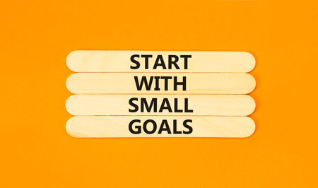 Start with small goals symbol. Concept words phrase Start with small goals on beautiful wooden stick. Beautiful orange paper background. Business Start with small goals concept. Copy space.の写真素材