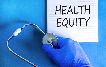 Health equity symbol. Concept words Health equity on beautiful white note. Doctor's hand in blue medical glove. Stethoscope. Beautiful blue background. Medical healthy lifestyle health equity conceptの写真素材