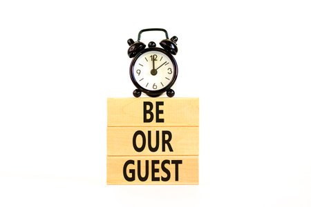 Be our guest symbol. Concept words Be our guest on beautiful wooden block. Black alarm clock....