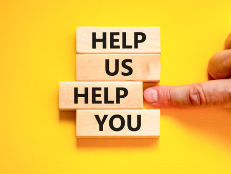 Help you symbol. Concept words phrase Help us help you on beautiful wooden blocks. Beautiful yellow paper background. Businessman's hand. Business Help you concept. Copy space.
