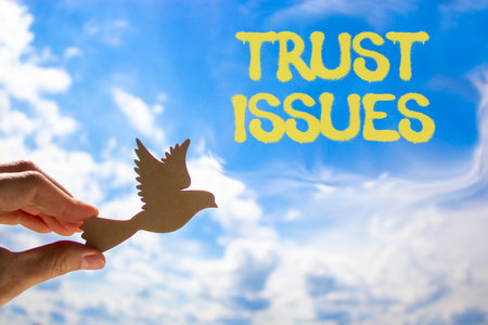 Trust issues symbol. Concept word Trust issues on beautiful blue sky. Businessman's hand with wooden...