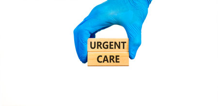 Urgent care symbol. Concept words Urgent care on beautiful wooden blocks. Doctor's hand in blue medical glove. Beautiful white background. Medical healthy lifestyle urgent care concept.の写真素材