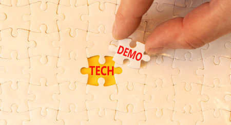 Tech demo symbol. Concept word Tech demo on beautiful white puzzles. Businessman's hand. Beautiful yellow paper background. Business tech demo concept. Copy space.の写真素材