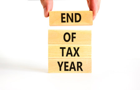 End of tax year symbol. Concept words phrase End of tax year on beautiful wooden blocks. Beautiful white paper background. Businessman's hand. Business End of tax year concept. Copy space.の写真素材