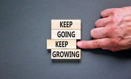 Keep going and growing symbol. Concept words phrase Keep going keep growing on beautiful wooden blocks. Beautiful gray background. Businessman's hand. Business Keep going growing concept. Copy space.の写真素材
