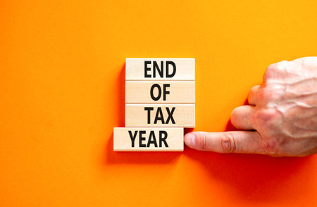End of tax year symbol. Concept words phrase End of tax year on beautiful wooden blocks. Beautiful orange paper background. Businessman's hand. Business End of tax year concept. Copy space.の写真素材