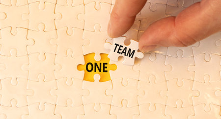 One team symbol. Concept word One team on beautiful white puzzles. Businessman's hand. Beautiful...