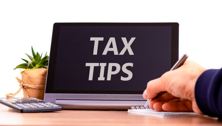 Tax tips symbol. Concept word Tax tips on beautiful black tablet. Businessman's hand with pen. Calculator. Beautiful white background. Business tax tips concept. Copy space.の写真素材