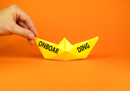 Onboarding success symbol. Concept word Onboarding on beautiful yellow paper boat. Beautiful orange background. Businessman hand. Business onboarding success concept. Copy space.の写真素材