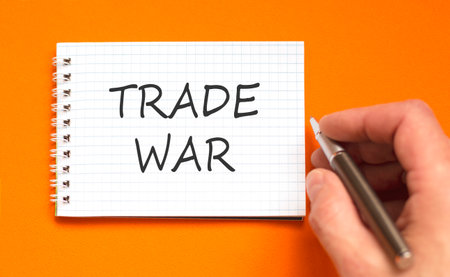 Trade war symbol. Concept word Trade war on beautiful white note. Businessman's hand with pen. Beautiful orange paper background. Business trade war concept. Copy space.の写真素材