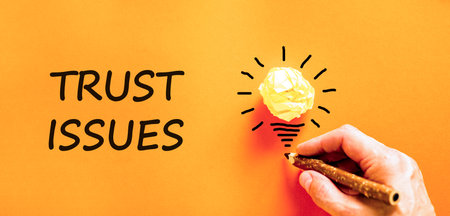 Trust issues symbol. Concept word Trust issues on beautiful orange paper. Businessman's hand. Light bulb icon. Beautiful orange paper background. Business trust issues concept. Copy space.の写真素材