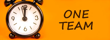 One team symbol. Concept word One team on beautiful orange paper. Beautiful black alarm clock....