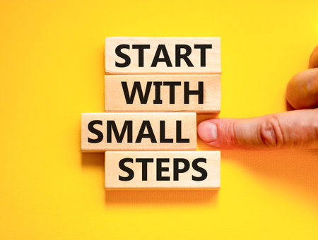 Start with small steps symbol. Concept words phrase Start with small steps on beautiful wooden blocks. Beautiful yellow background. Businessman hand Business Start with small steps concept. Copy spaceの写真素材