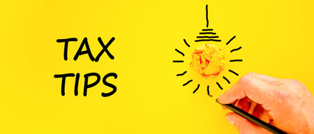 Tax tips symbol. Concept word Tax tips on beautiful yellow paper. Businessman's hand. Light bulb...