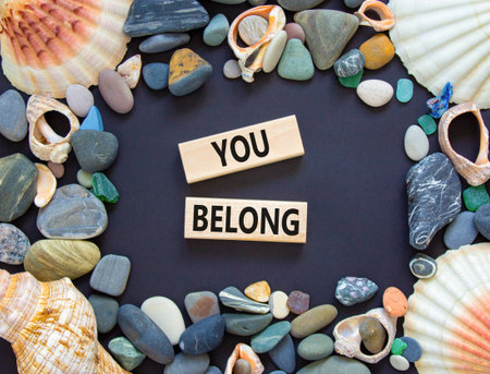 Belonging and you belong symbol. Concept words You belong on beautiful wooden blocks. Beautiful black background. Beautiful sea stones shell. Business belonging and you belong concept. Copy space.の写真素材