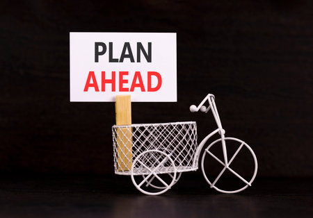Plan ahead symbol. Concept word Plan ahead on beautiful white paper. Beautiful wooden clothespin. Miniature white bicycle. Beautiful black background. Business plan ahead concept. Copy space.の写真素材