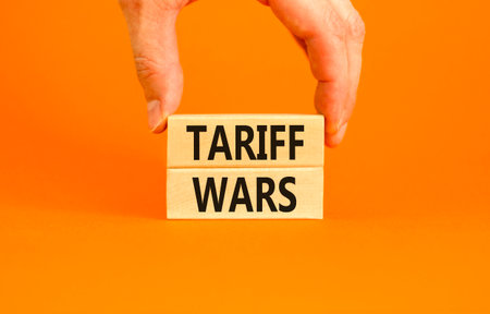 Trade tariff wars symbol. Concept word Tariff wars on beautiful wooden blocks. Beautiful orange paper background. Businessman's hand. Business trade tariff wars concept. Copy space.の写真素材